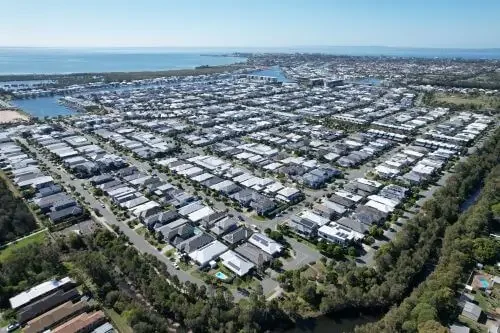 Aerial view of Newport masterplanned community with multiple rows of houses, streets, and greenery near the ocean.