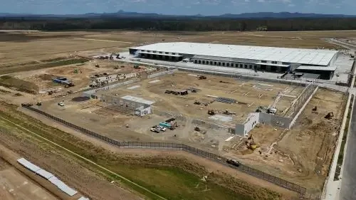 Construction site with industrial building with ongoing building work, equipment, and vehicles on the ground.