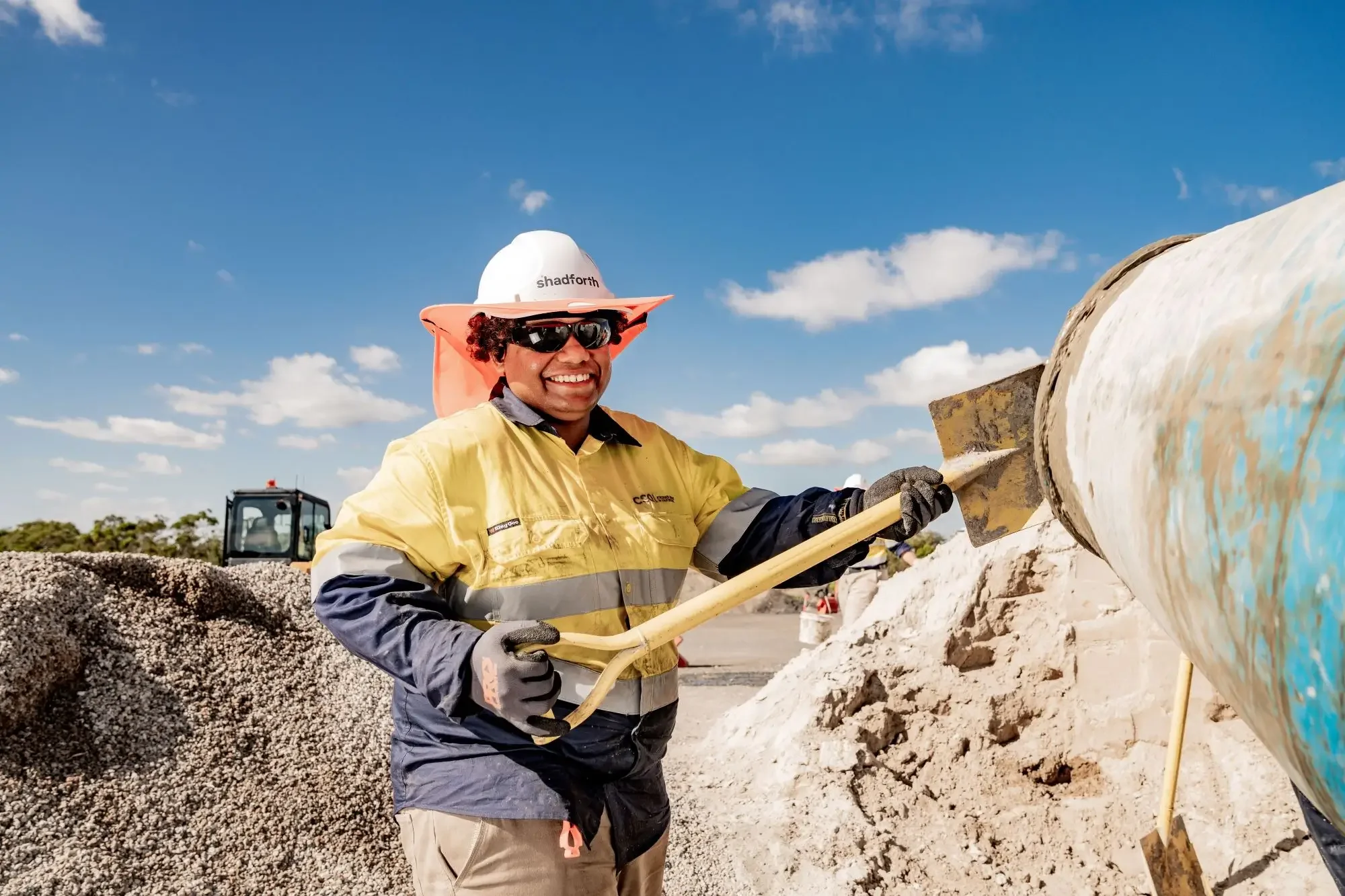 A construction worker in a yellow hi vis shirt, wearing hard hat and holding a shovel.