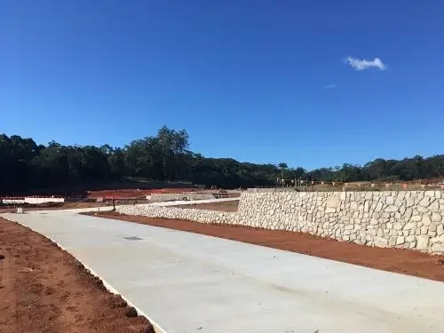 Construction site with concrete pavement and stone retaining walls under a clear blue sky.