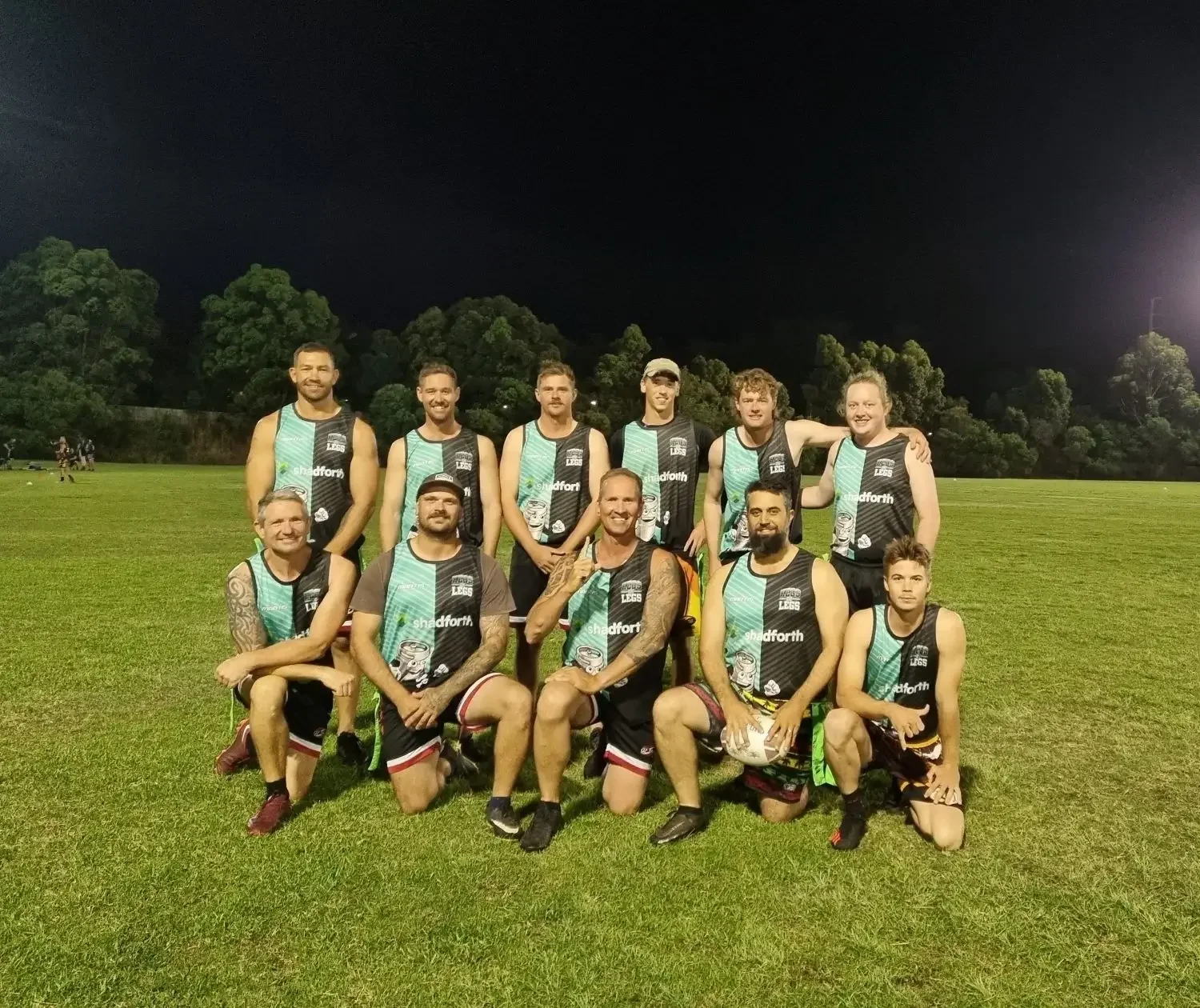 A group of men wearing Shadforth singlets. They are posing for a photo on grass.