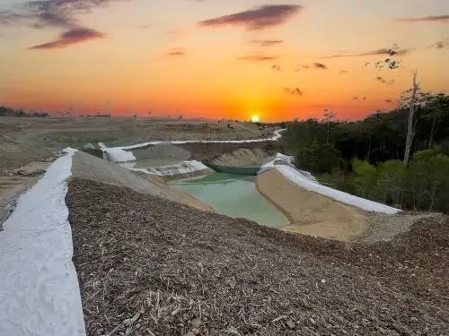 Drainage pond with white lining at sunset, surrounded by earth and trees