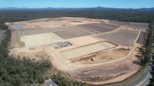 Aerial view of a construction site with cleared land, dirt roads, and building foundations, surrounded by trees.