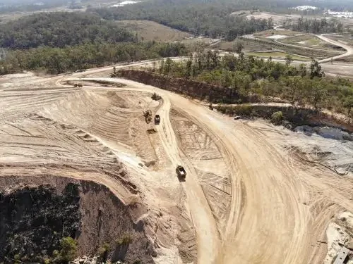 Aerial view of a construction site with machinery, dirt and trees in the background.