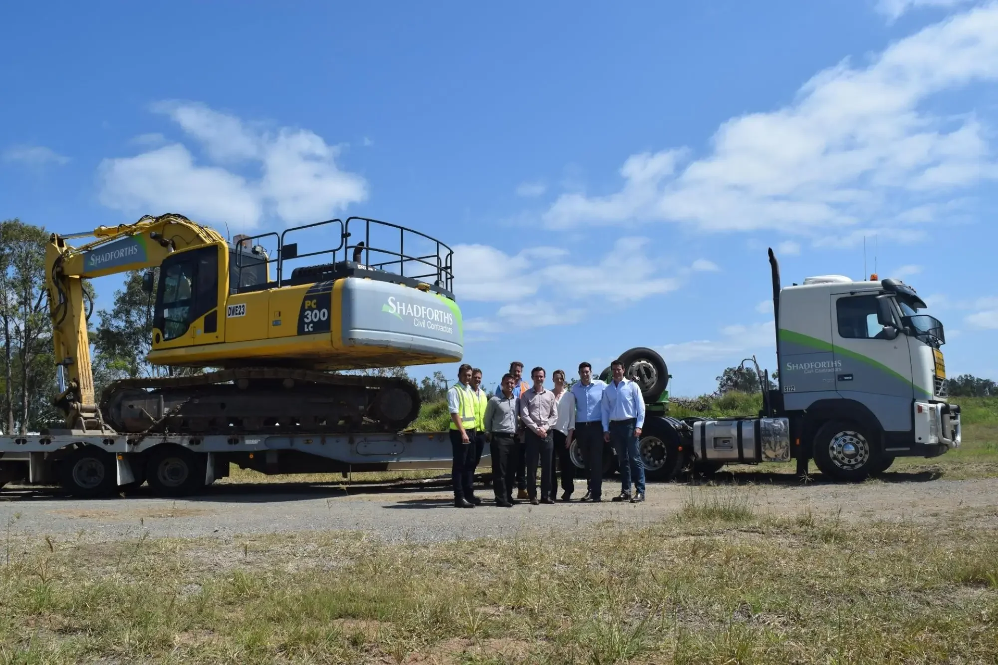 Shadforth team standing beside an excavator on a float and heavy haulage truck at a civil construction site.