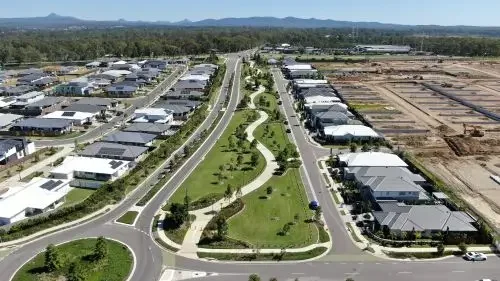 Aerial view of Everleigh Precinct with modern houses, a central landscaped park with walking paths, and wide roads, with mountains in the background.