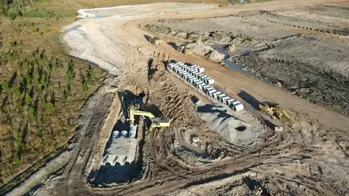 Drone view of underground drainage installation with precast concrete pipes, excavators and earthworks on a construction site.