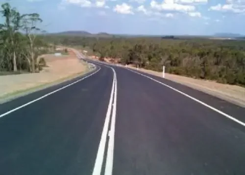 Newly completed road through a residential development with fresh asphalt and surrounding earthworks.