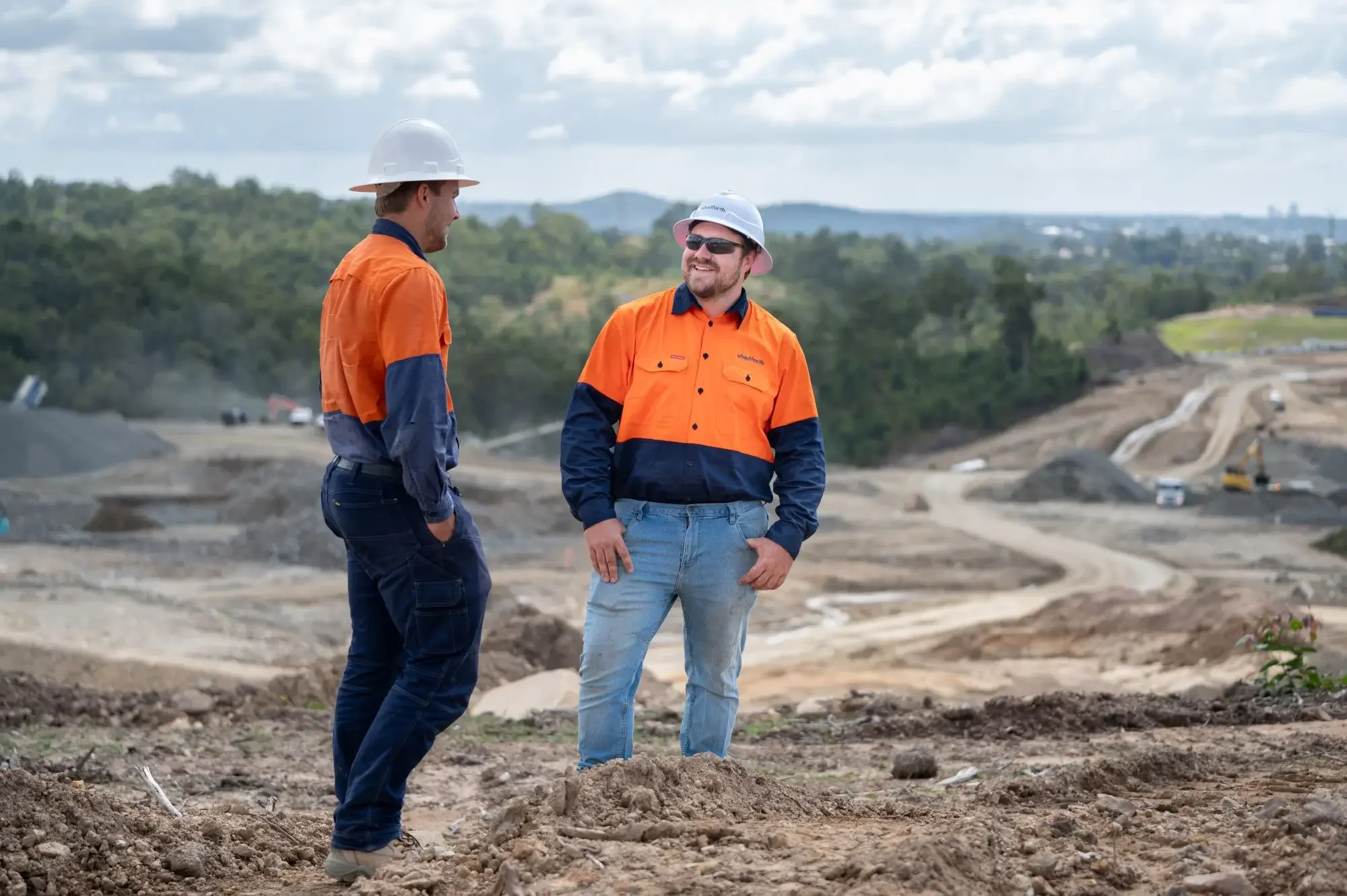 Two construction workers in orange hi-vis shirts stand on a hill, overlooking and discussing works across the SkyRidge project.