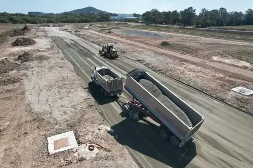 Image of a construction site with a truck dropping gravel on a roads that's being constructed.
