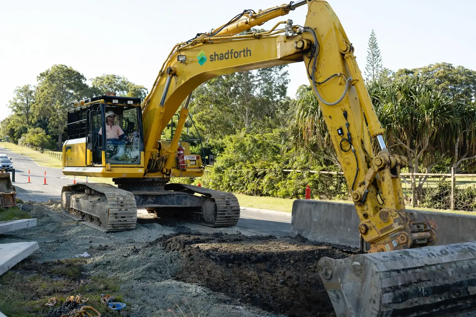 yellow excavator with the Shadforth logo and a man sitting in it. Digging up a road.