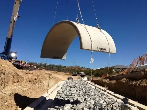 Crane installing a large precast concrete culvert during drainage infrastructure construction on a mining project.