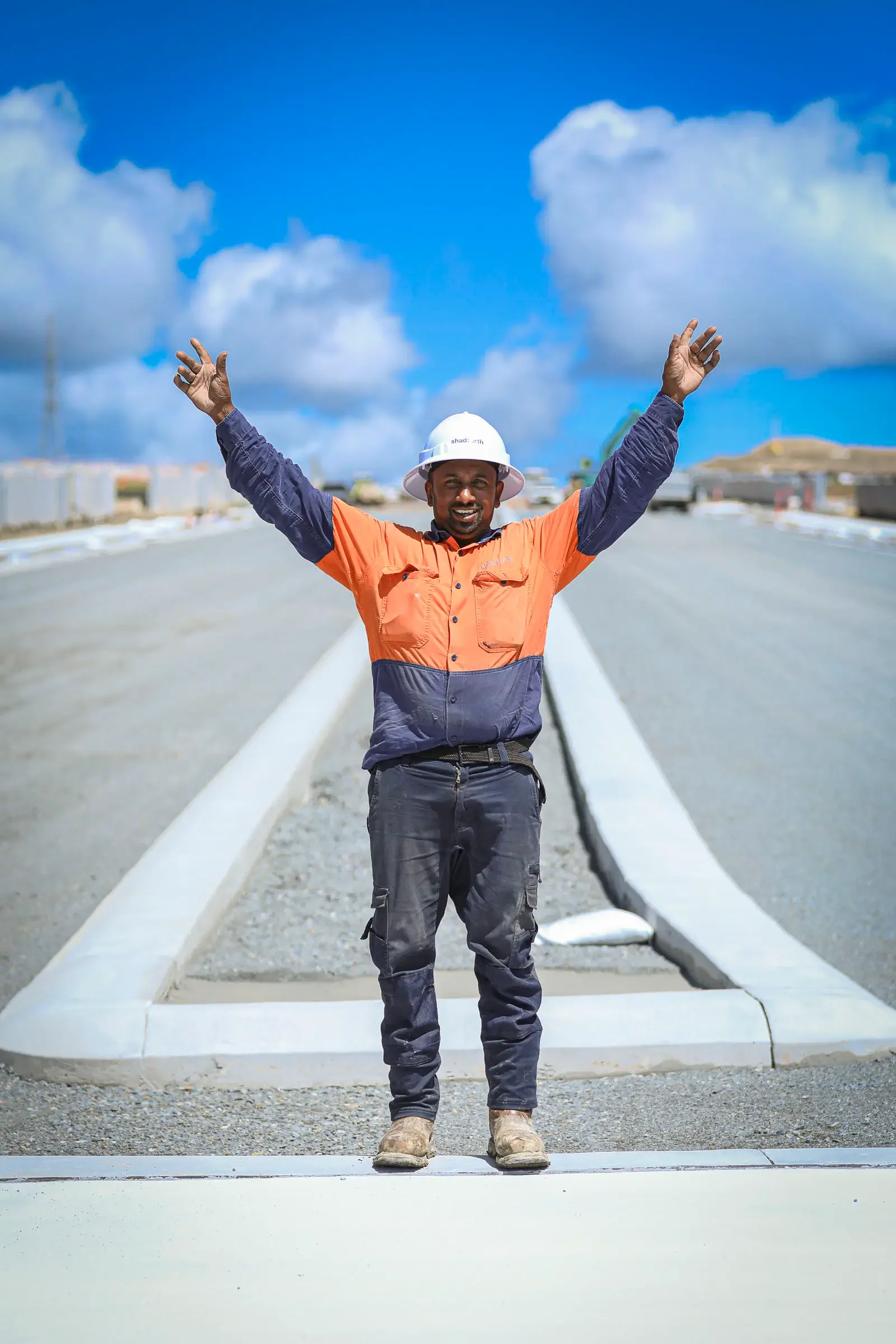 Construction worker standing in the middle of a construction site, wearing safety gear raising his arms.