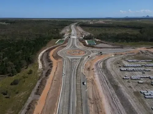Aerial view of Bells Creek Arterial construction project with multiple lanes, roundabout, surrounding construction sites, trees and open land.