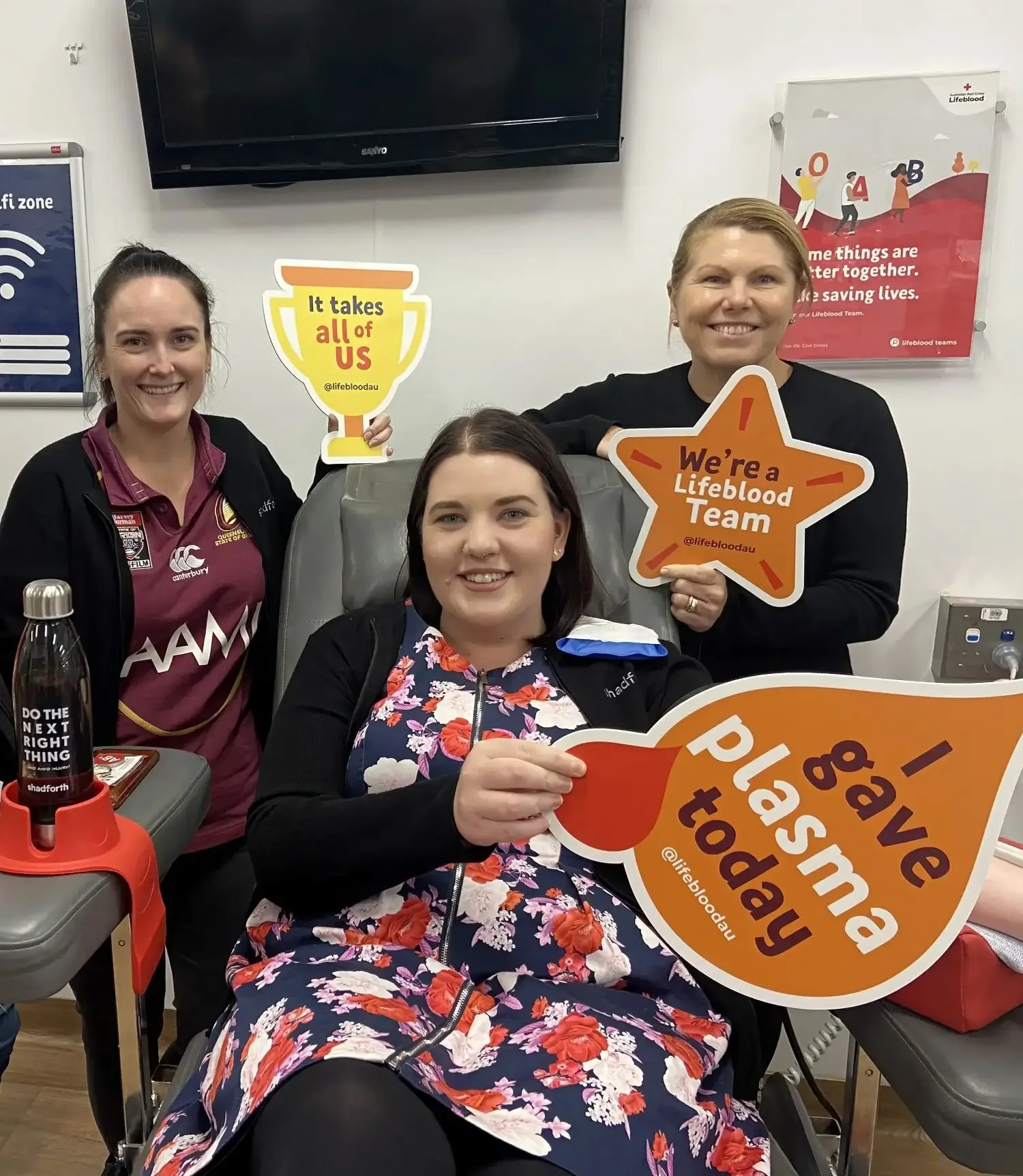 Three women smiling while holding blood donation signs.