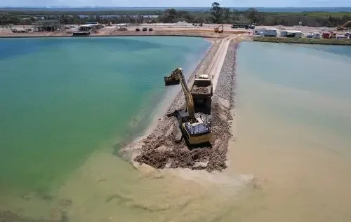 Construction excavator on a barge working on a canal or flood control project with water on both sides.