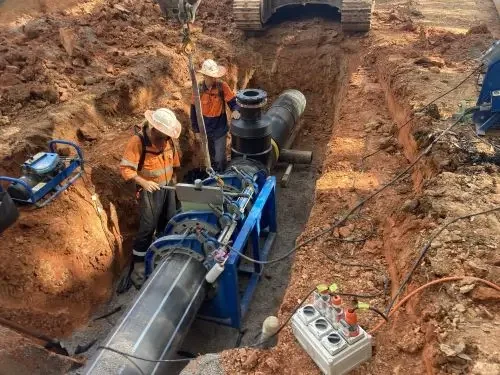 Two workers in safety gear and hats inspecting a large underground pipeline being installed in a trench.