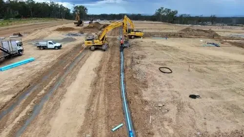 Construction site with heavy machinery installing large blue pipes into the ground.