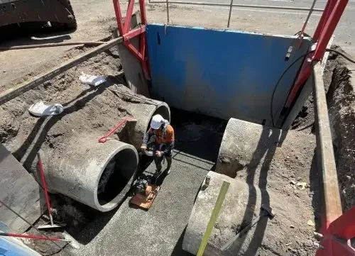Worker installing concrete into a large underground pipe at a construction site.