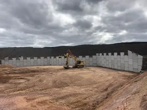 Excavator working beside precast concrete retaining walls during civil construction on a large infrastructure project.
