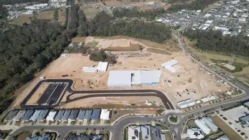 Aerial view of a construction site with cleared land, some buildings, and a winding road in a residential area.