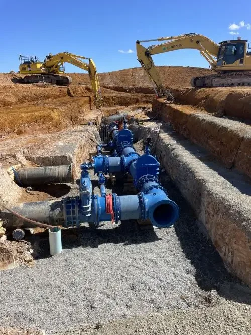 Excavators install large-diameter water mains and valves within a deep trench on a civil construction project.