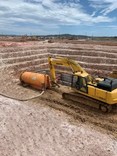 Excavator works inside a stepped excavation during construction of major underground water infrastructure.