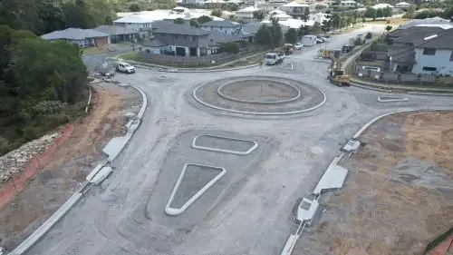 Image of a road and round about under construction. Houses in the background.