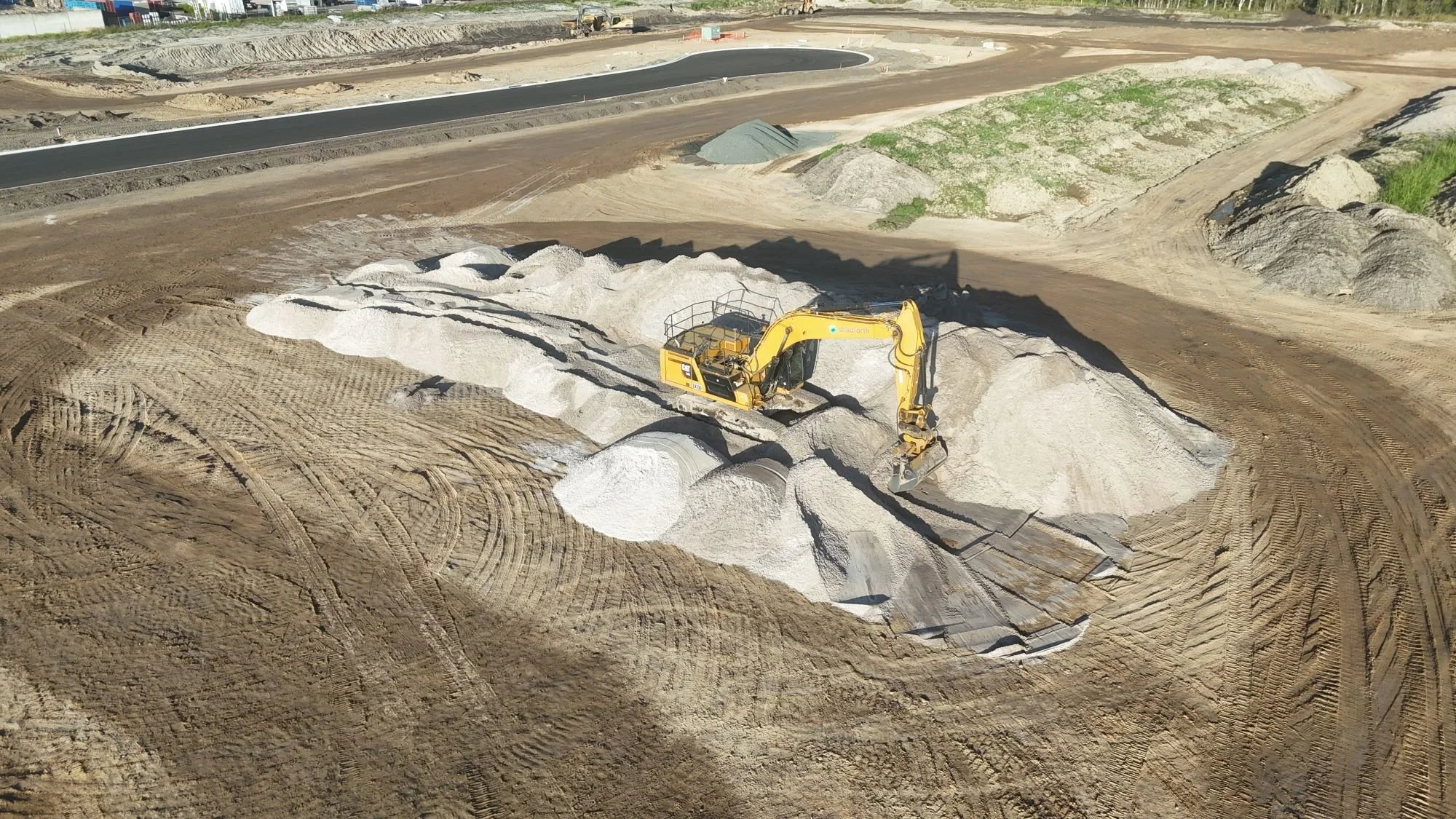Aerial view of a Shadforth excavator loading aggregate stockpiles on a civil construction site with newly formed roads and earthworks in the background.