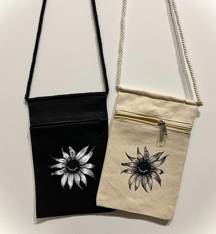 Cotton crossbody pouches featuring a smiling sunflower graphic in black and natural colors.