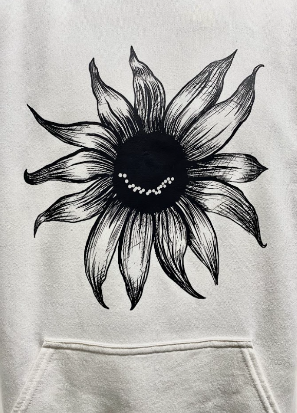 White hoodie close-up shot featuring a smiling sunflower graphic on the front