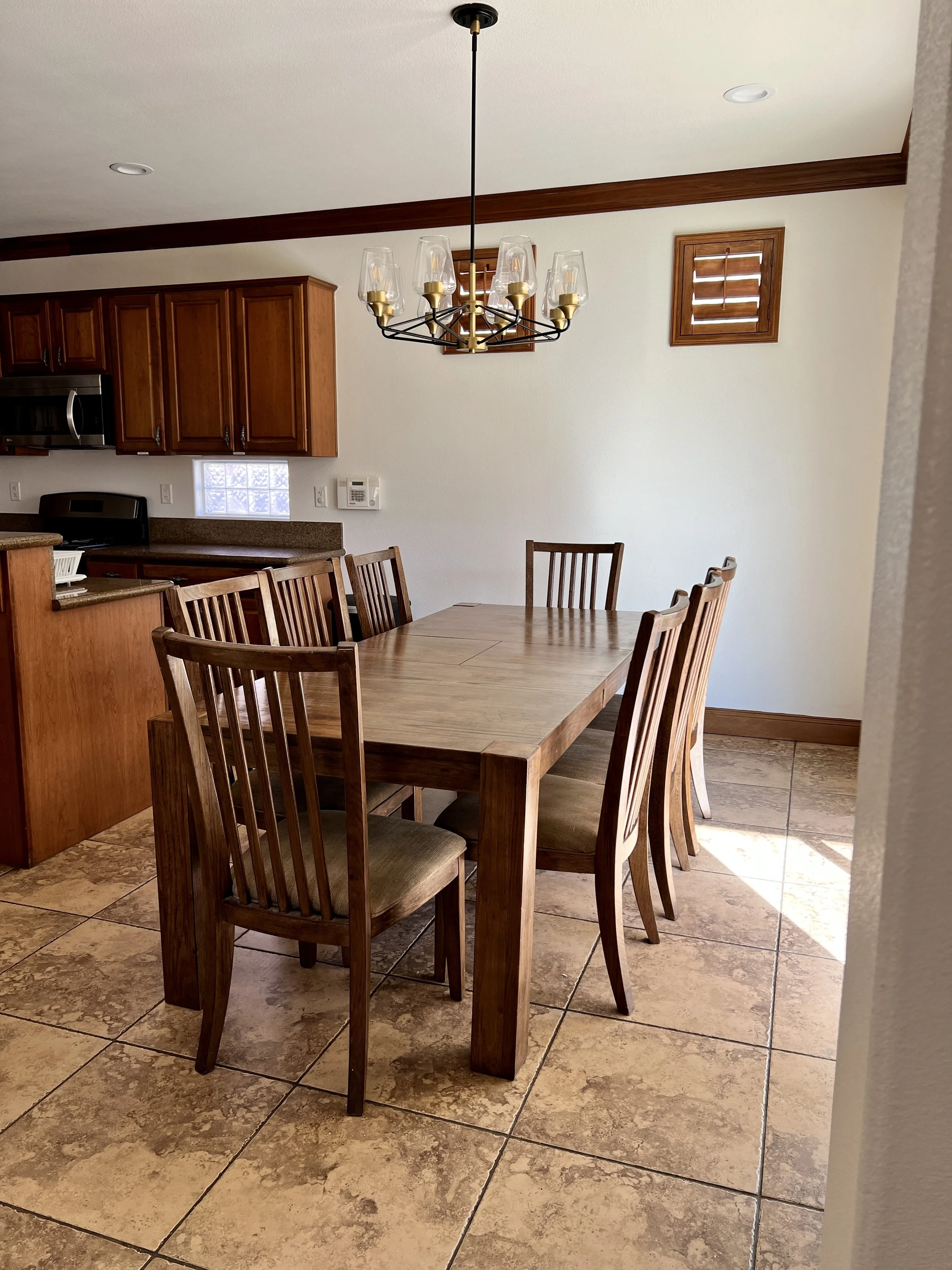 Wooden dining table with six matching chairs in a room with tiled floor and overhead chandelier