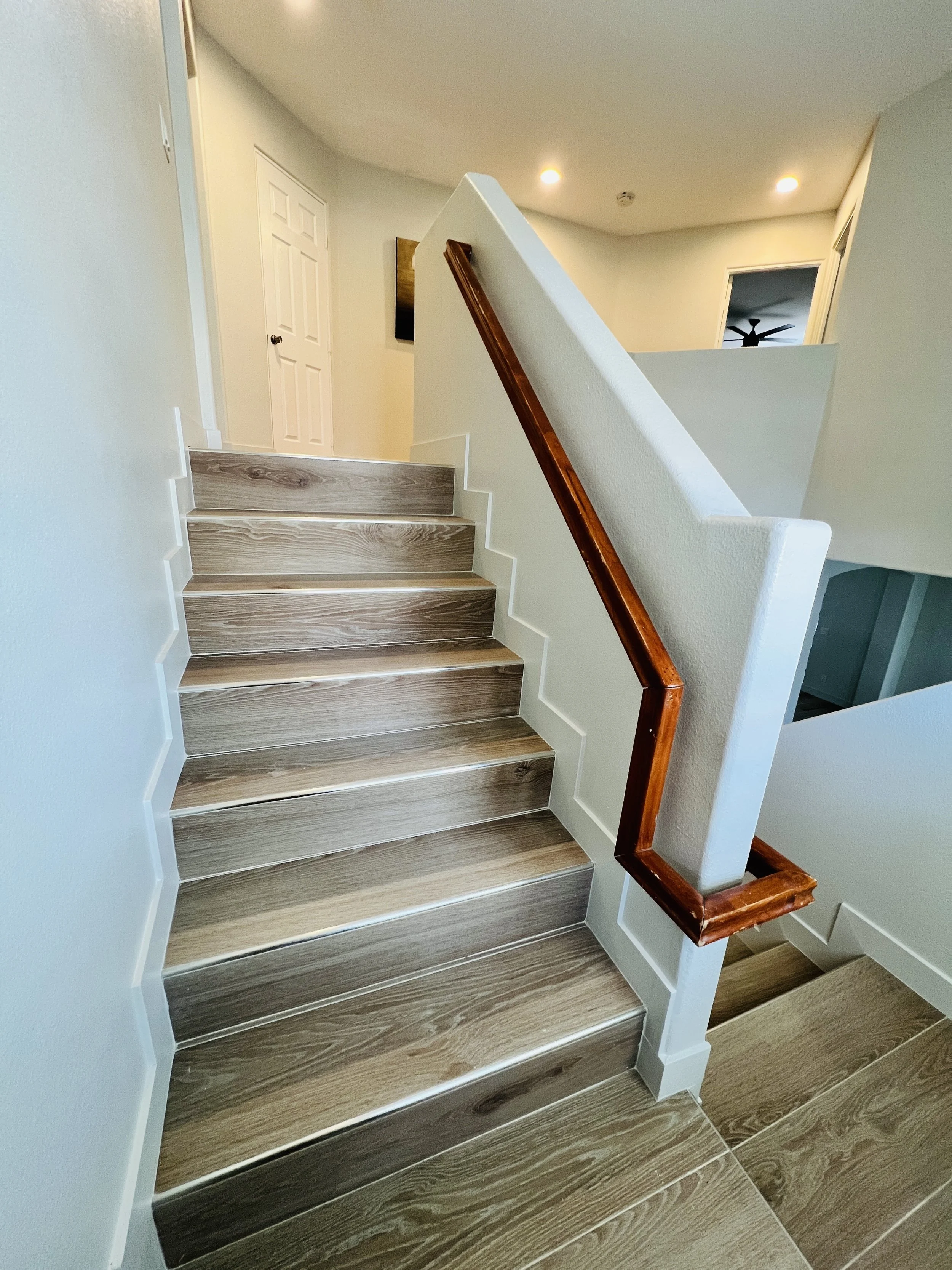 Wooden staircase with white walls and a dark wooden handrail, leading to a landing with a door and a hallway.