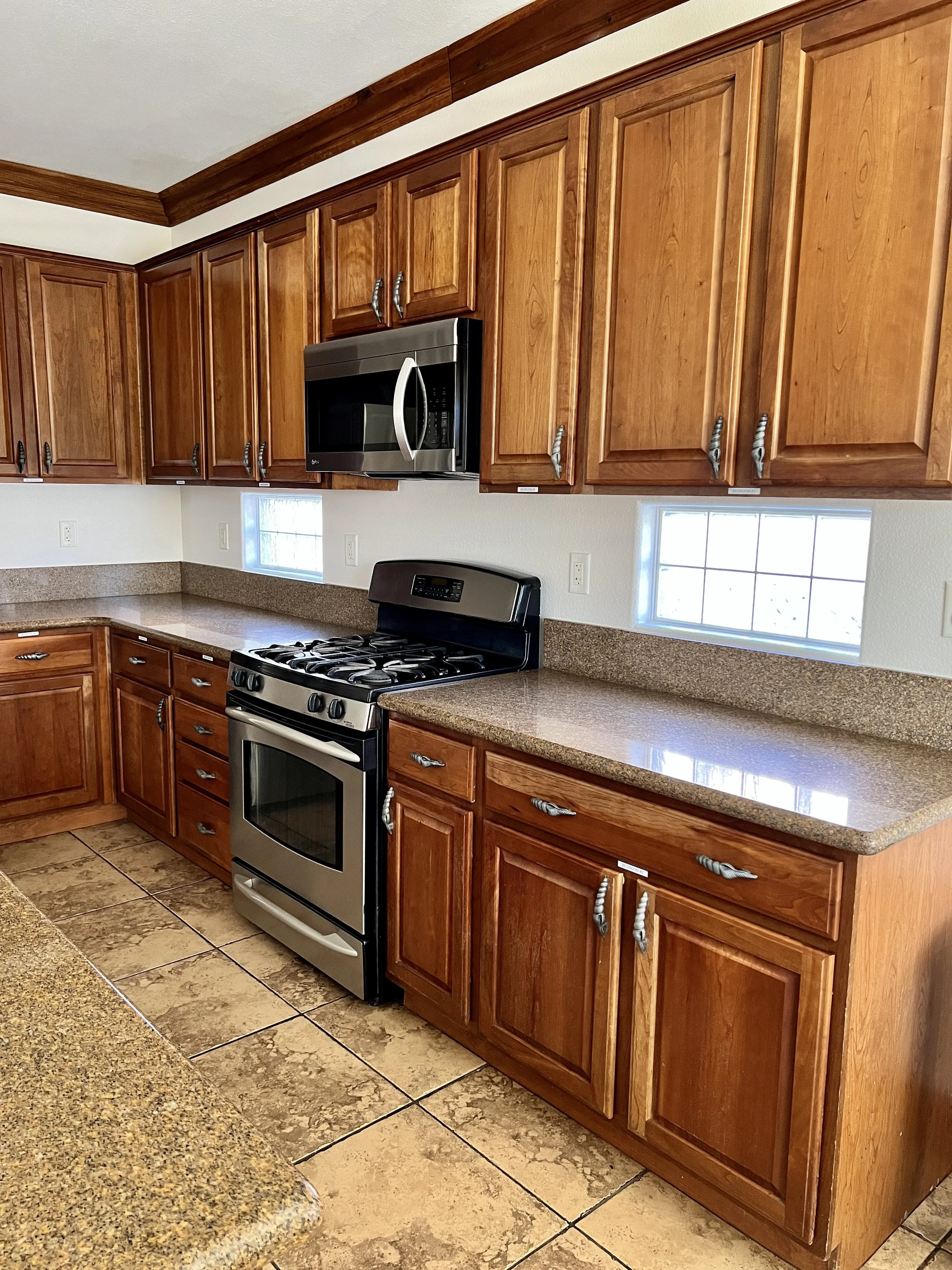 Kitchen with wooden cabinets, granite countertops, a stainless steel microwave, and a stove, with two small windows above the countertop.