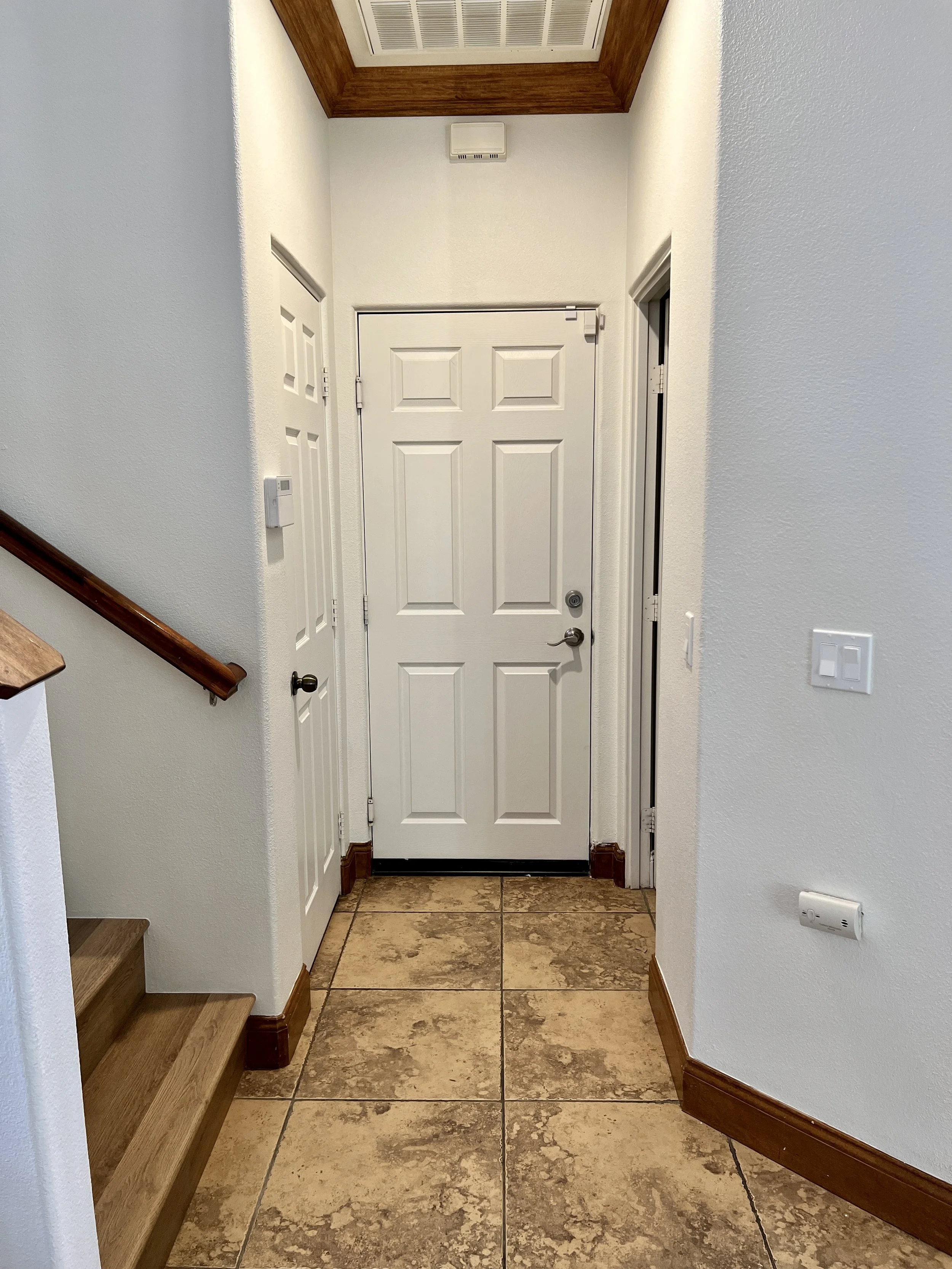 Entrance foyer with a white front door, stone tile flooring, and staircase on the left with wooden handrail.