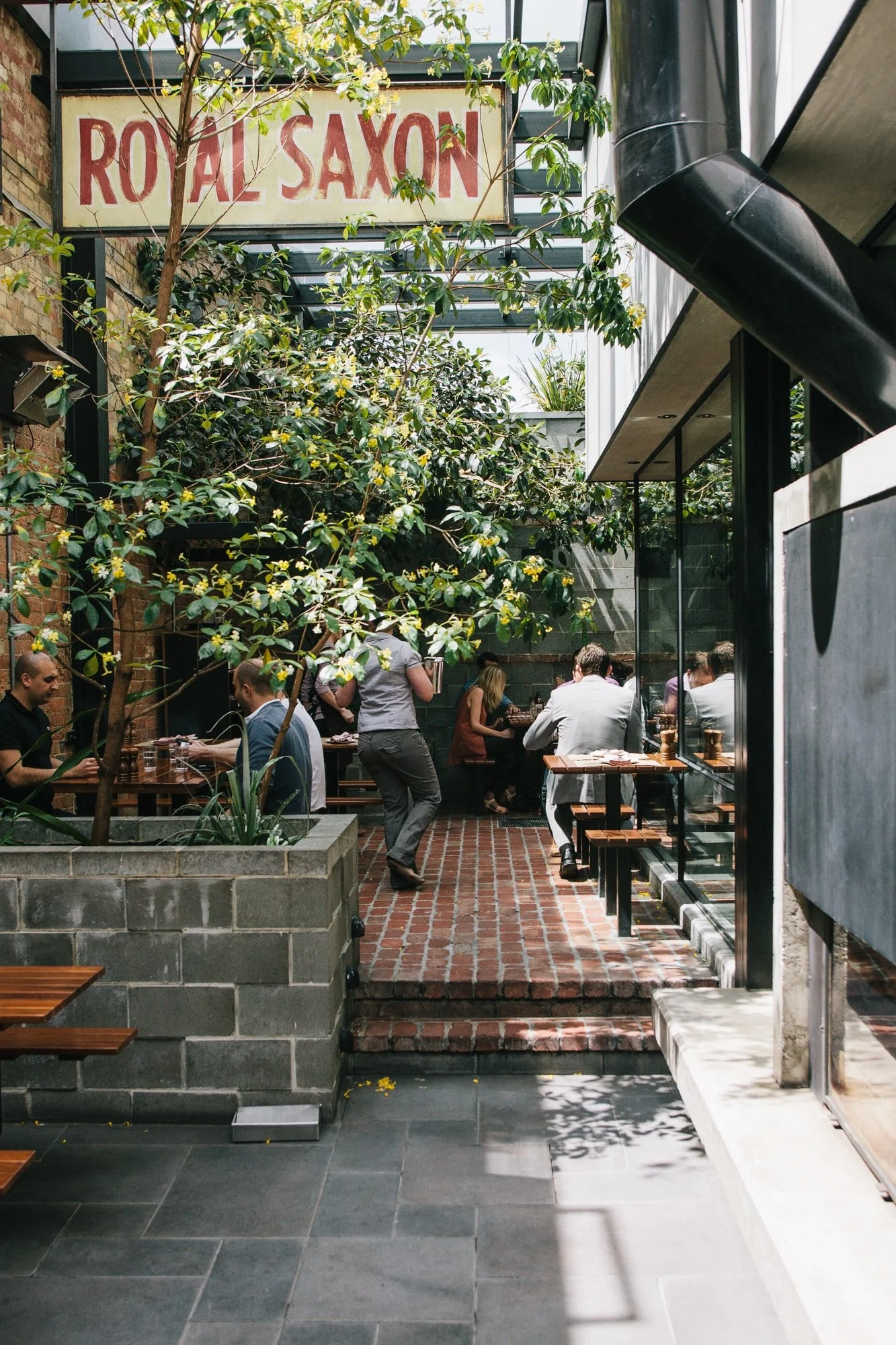 Outdoor patio of a restaurant called Royal Saxon with people dining, greenery, and a vintage sign overhead.