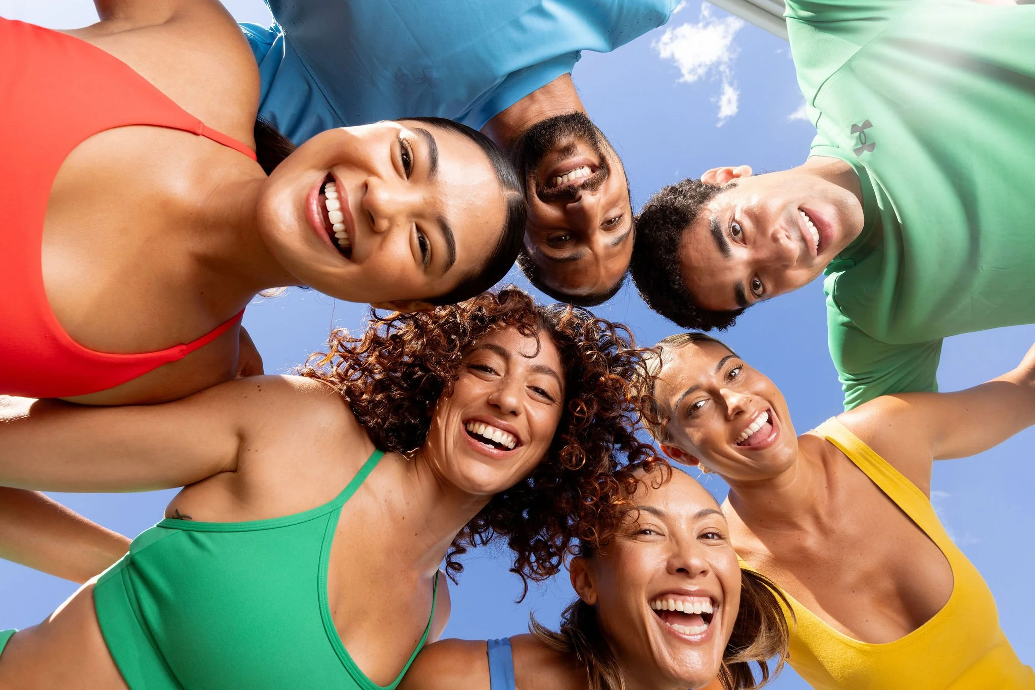 Group of seven people smiling and looking down toward the camera, taken outdoors against a blue sky.