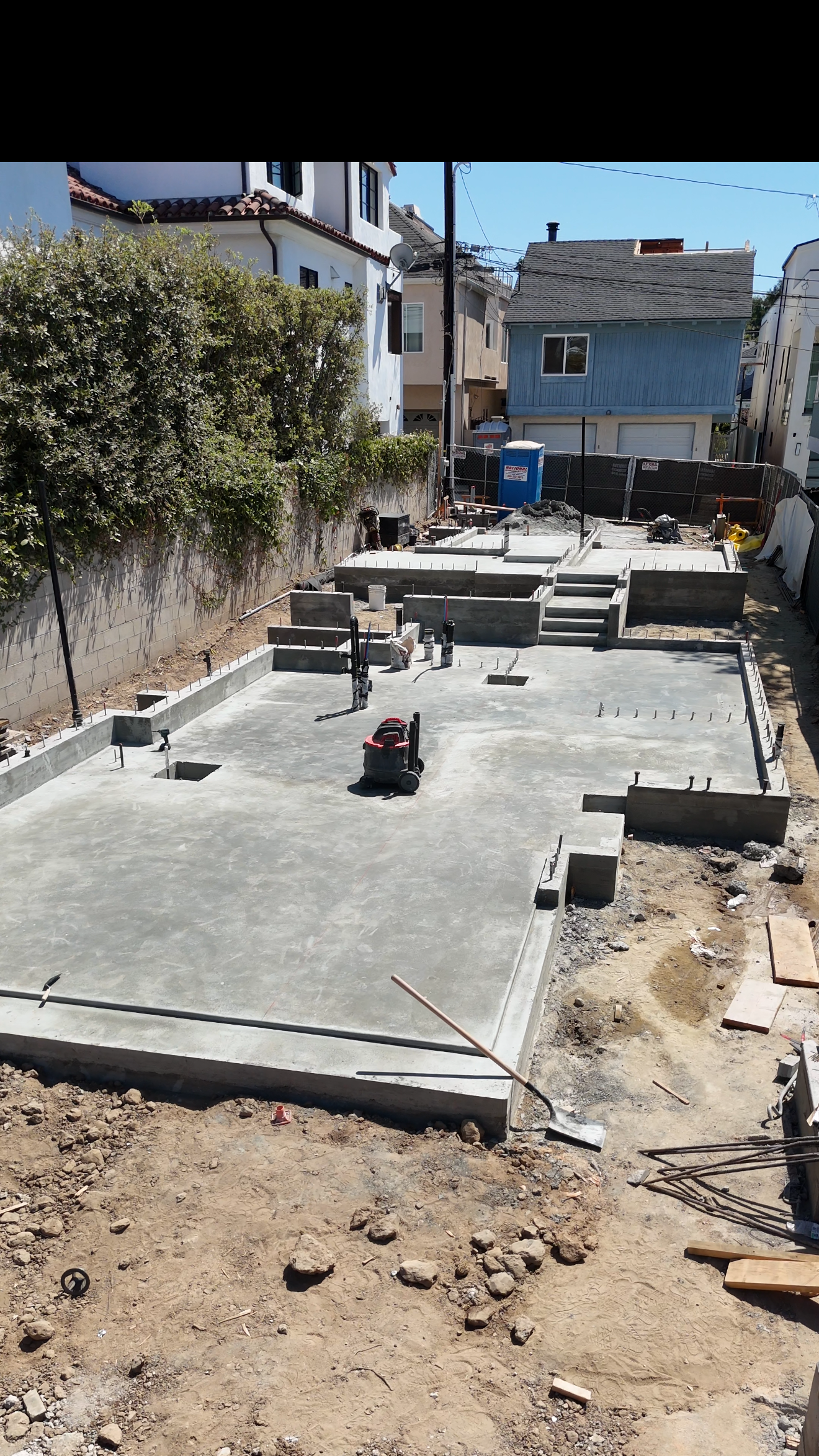Construction site with freshly poured concrete foundation, nearby houses, and construction tools.