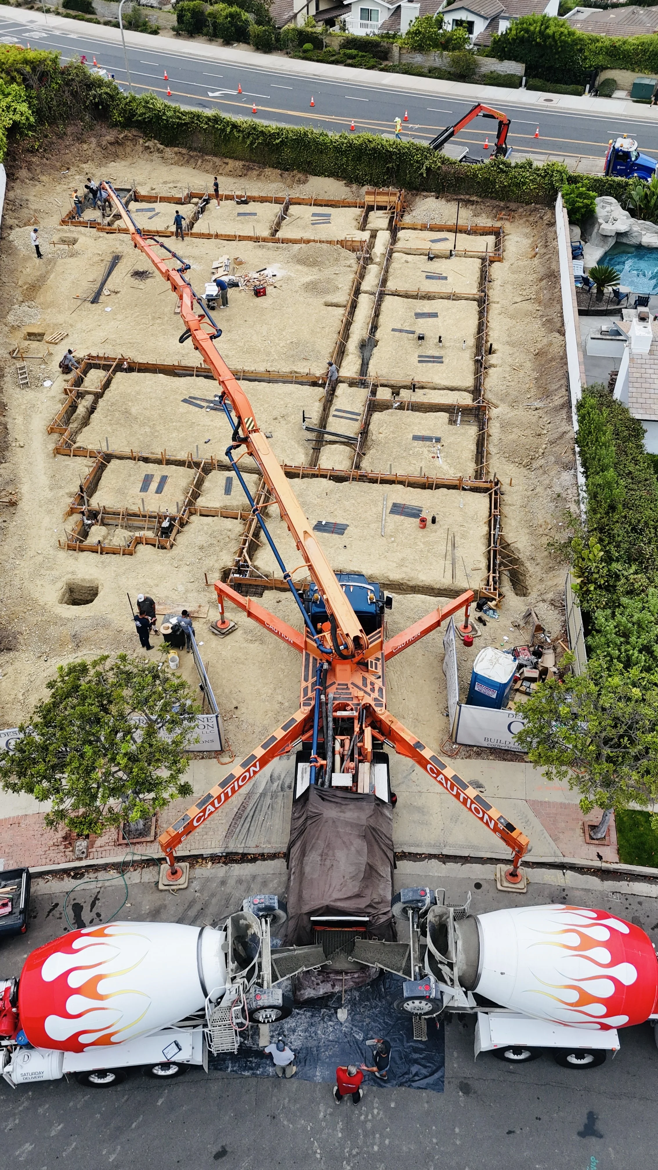 Construction site with a concrete mixer truck and a crane pouring cement into foundation forms, with workers overseeing the process.