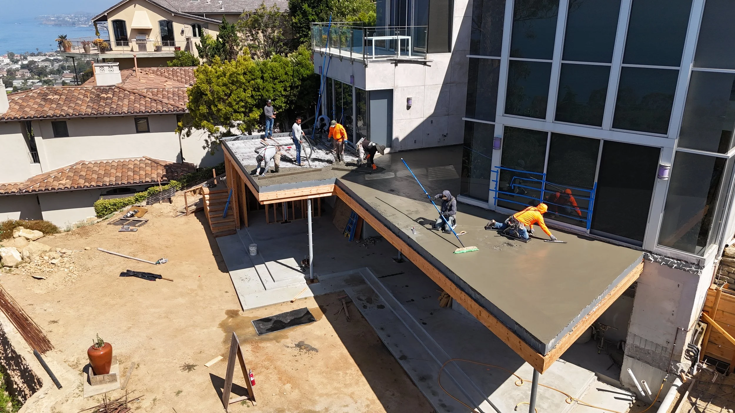 Construction workers pouring and leveling concrete on a modern building's outdoor terrace, with some workers spreading the concrete and others overseeing the work.