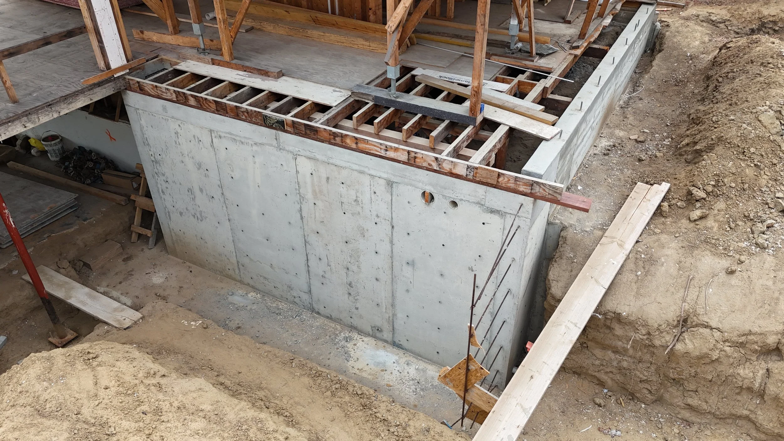 Construction site showing a concrete foundation with wooden framing and scaffolding for a building under construction.