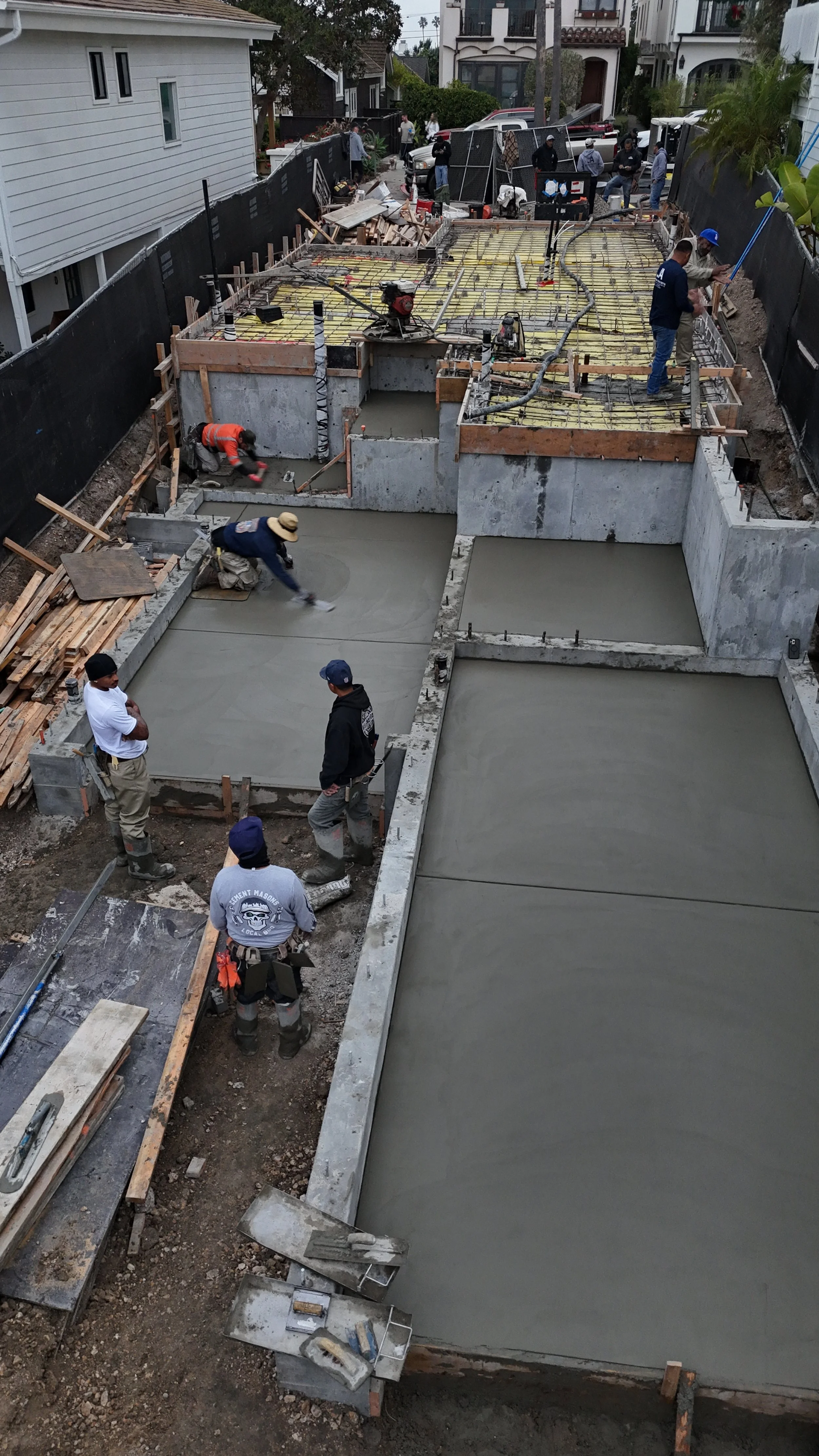 Construction workers pouring and smoothing concrete for a building foundation in a residential neighborhood.