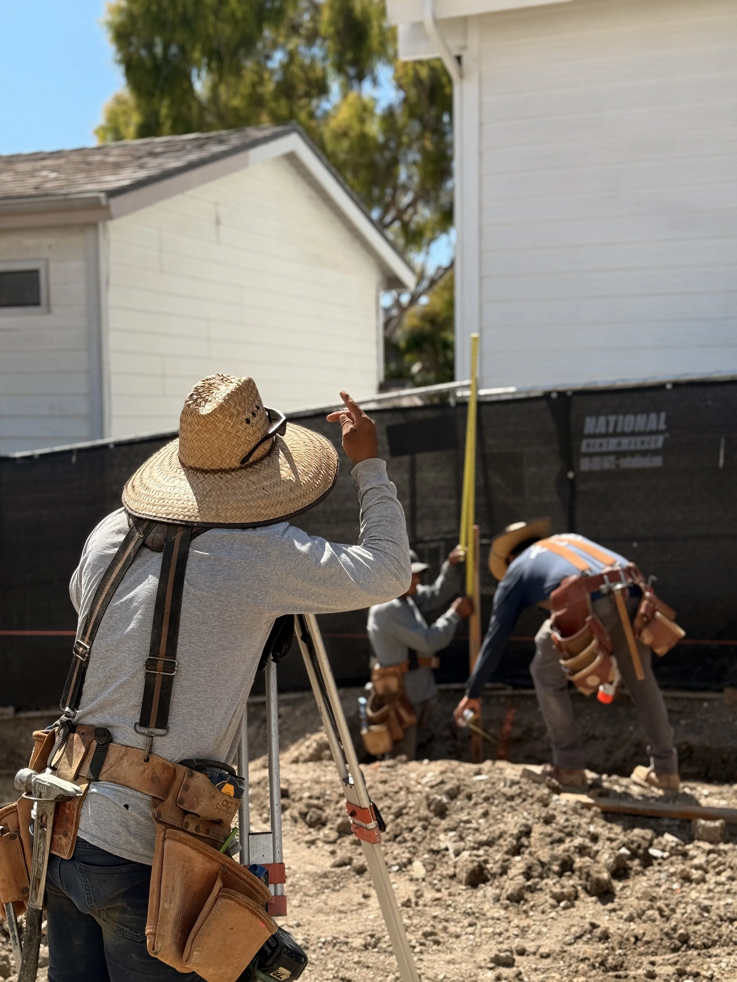 Construction workers measuring and working on a building foundation on a sunny day.