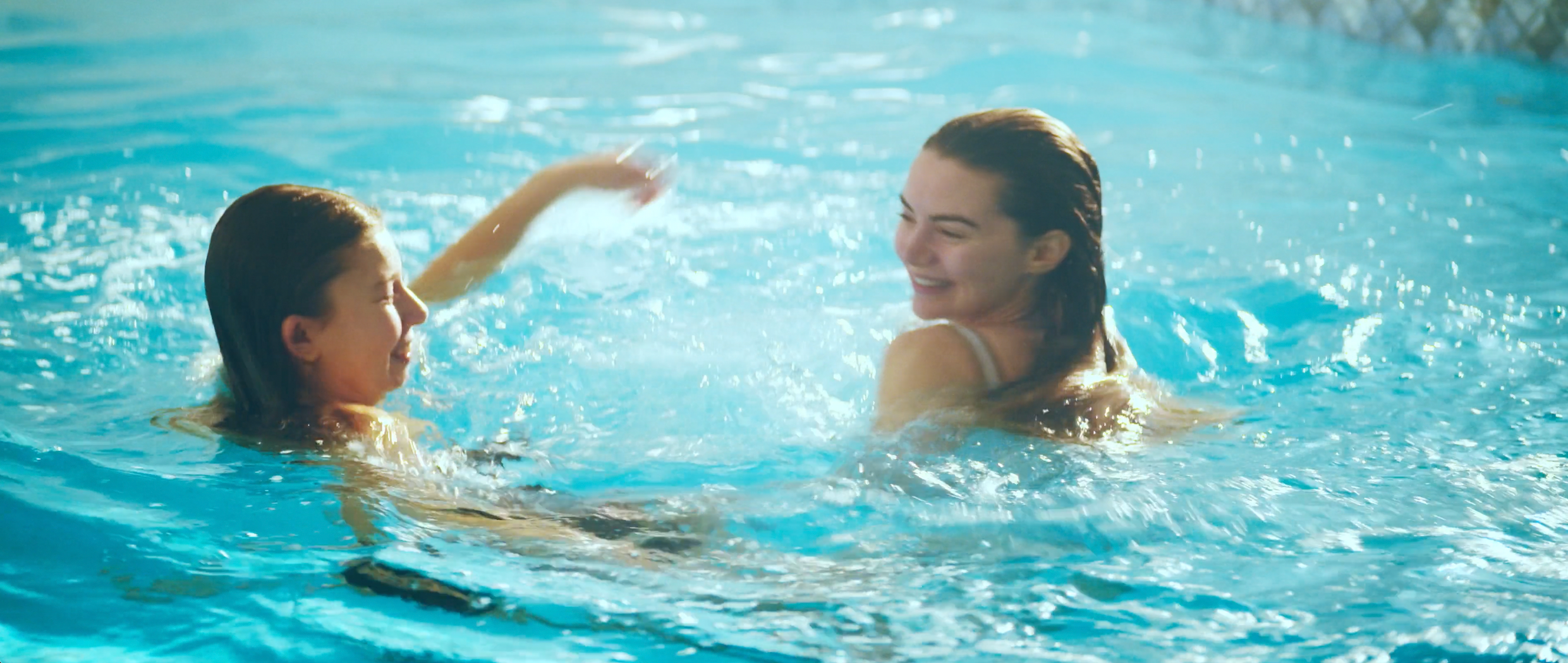 Two women swimming and playing in a swimming pool, smiling and enjoying their time.