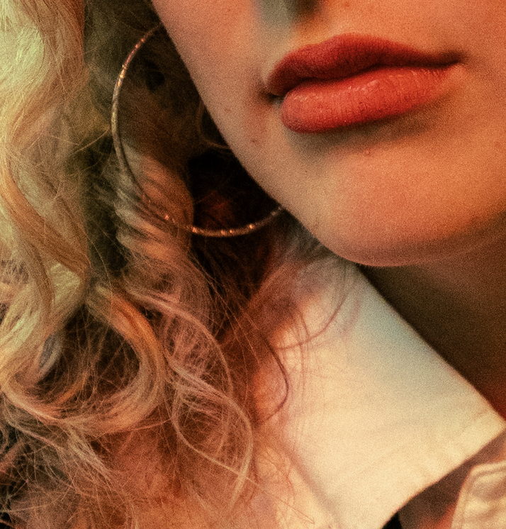 Close-up of a woman's lips with orange lipstick, gold hoop earring, and curly blonde hair.