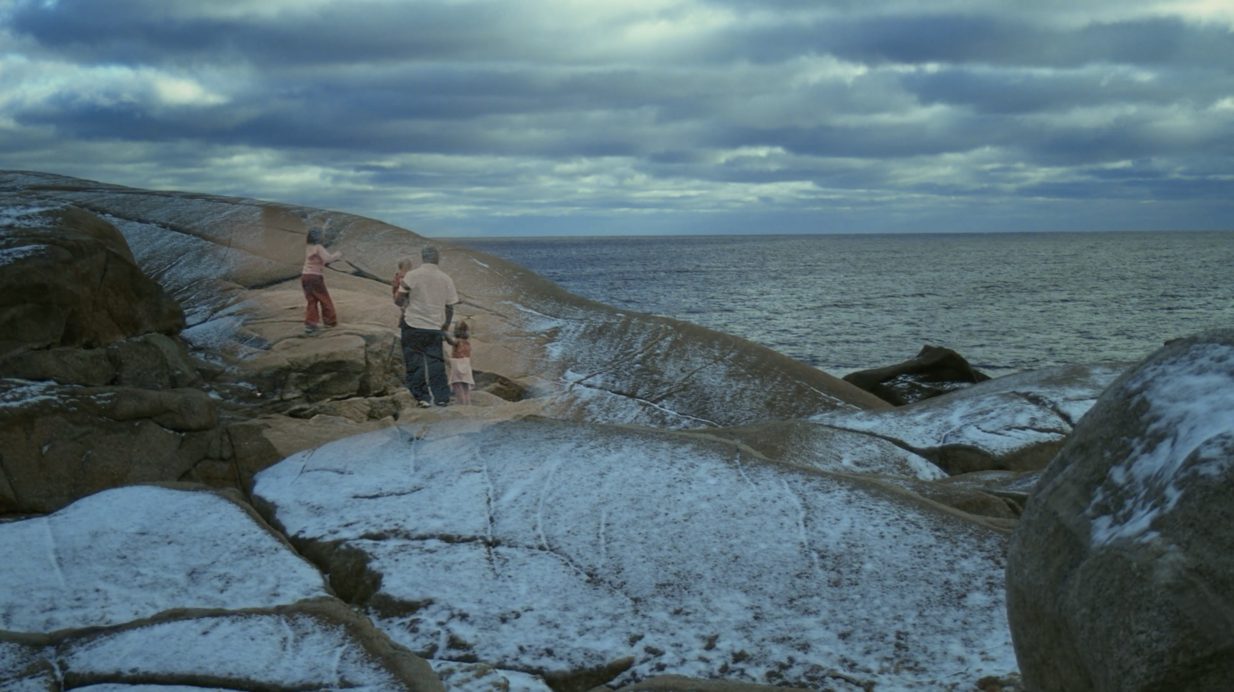 Family of five on rocks by the ocean under a cloudy sky during daytime.