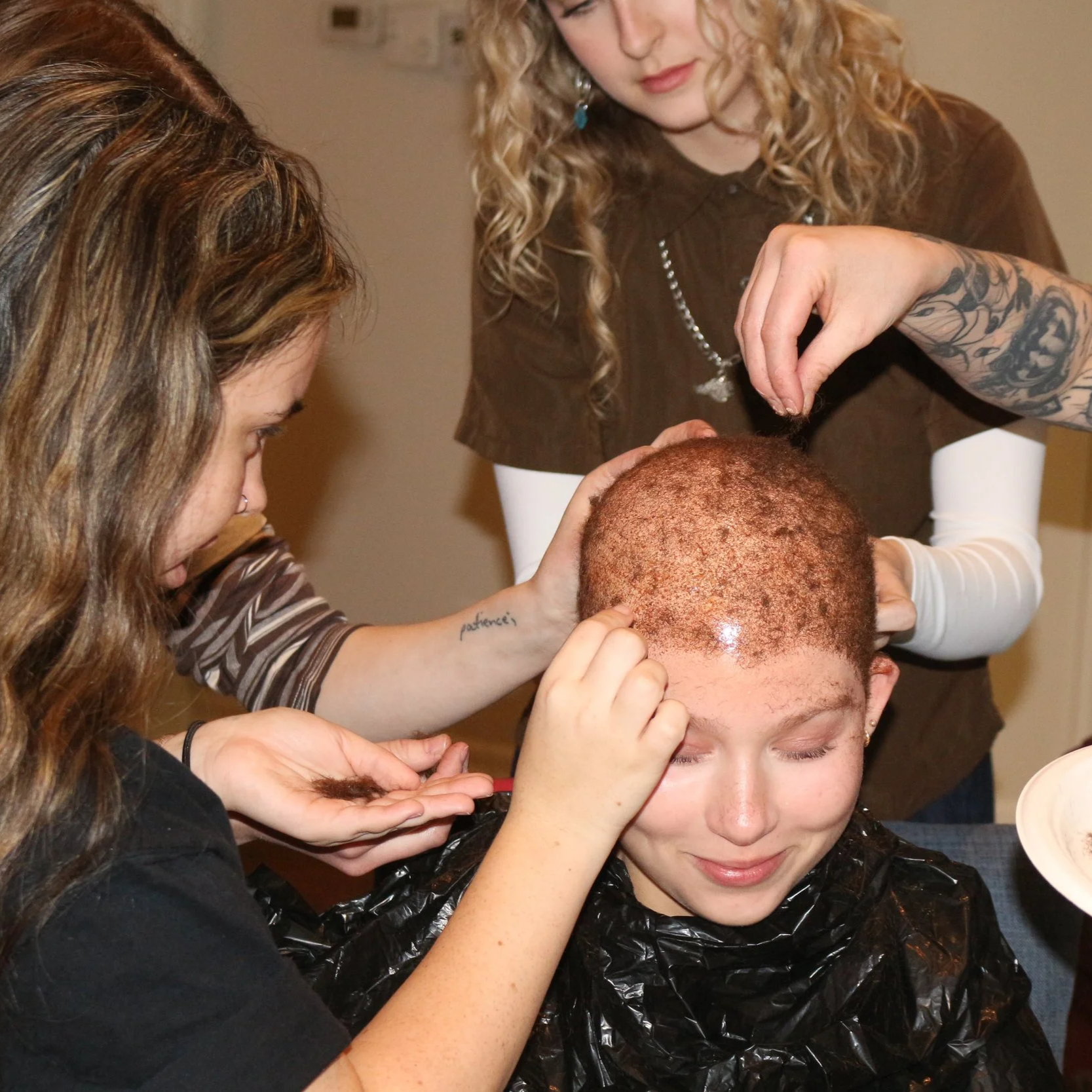 A person getting a short, curly hairstyle applied by two hairstylists in a salon.