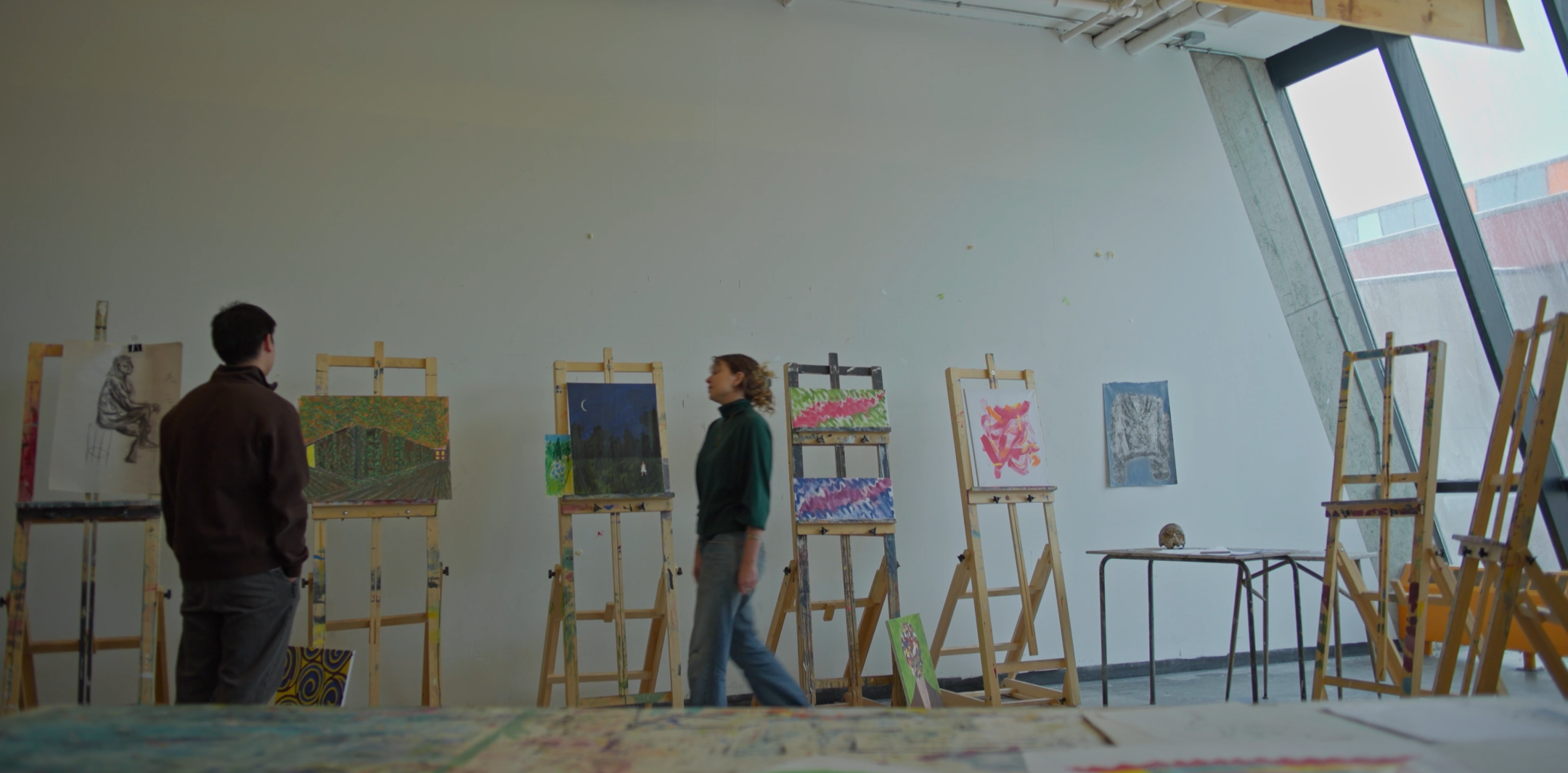 Two people viewing artwork in an art gallery with paintings on display on easels.