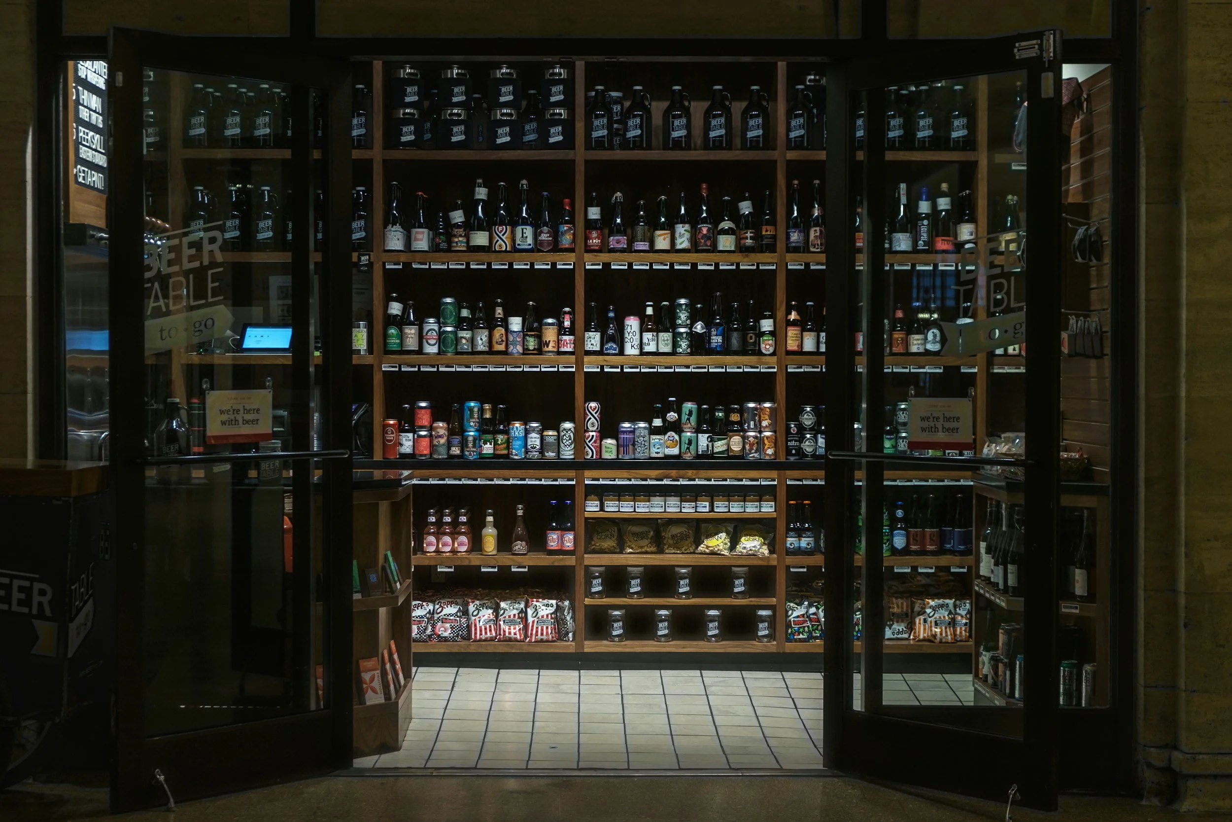 A glass door beer display case filled with various bottled beers and cans inside a store.