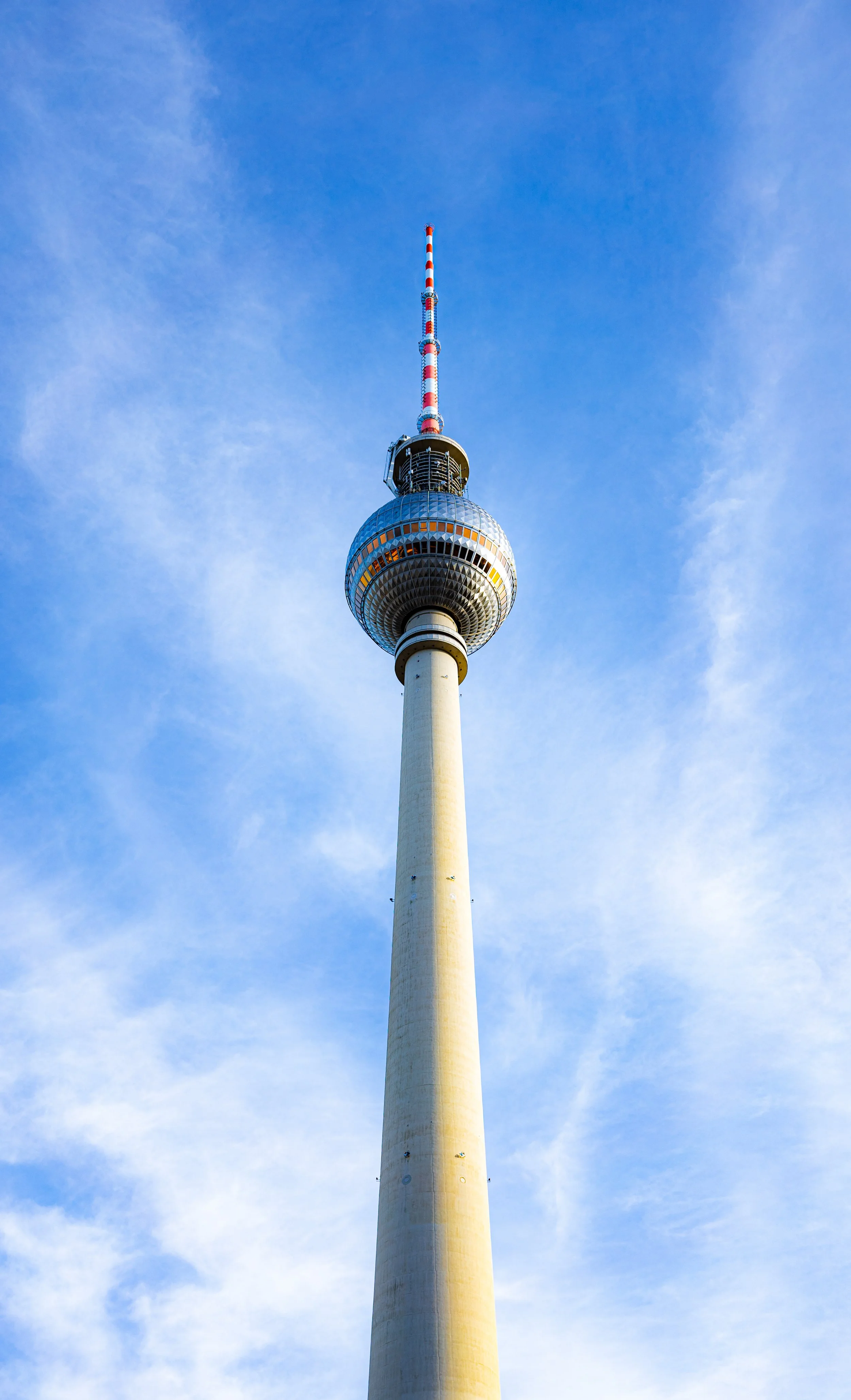 View of Berlin TV Tower against blue sky with wispy clouds.